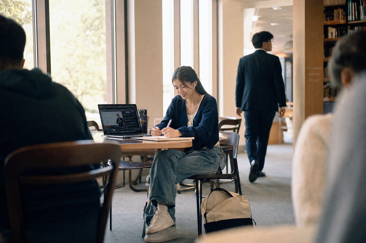 A job seeker takes notes while watching a course video in a sunlit library